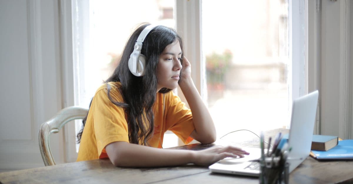 Aluna ouvindo música de fones para aprender inglês — 8 músicas para alunos de nível avançado-intermediário